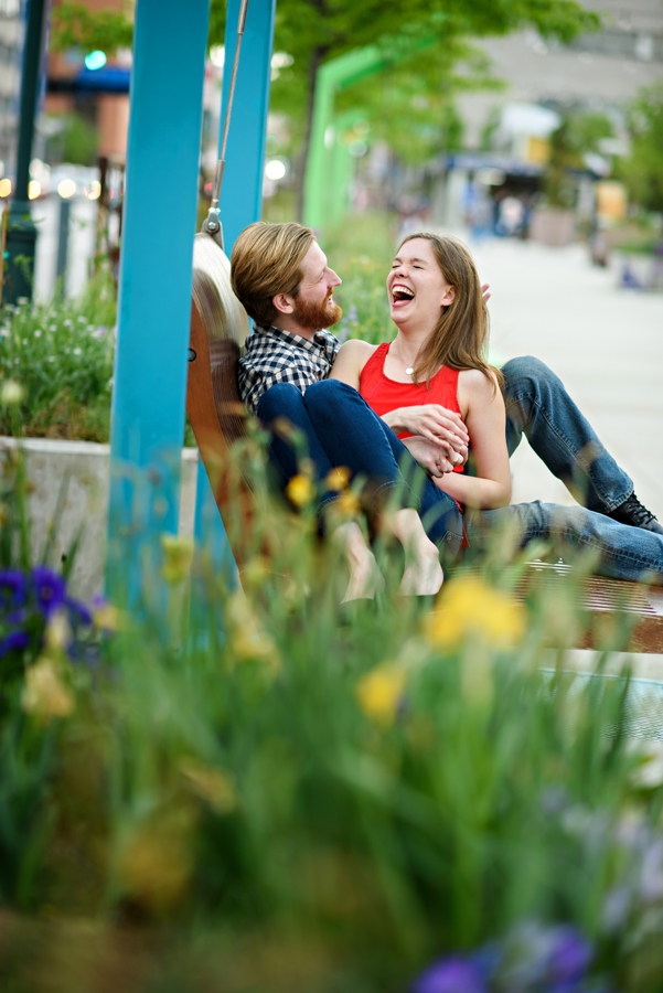 A man making his girlfriend laugh on the swings outside of 30th street station during their engagement session.